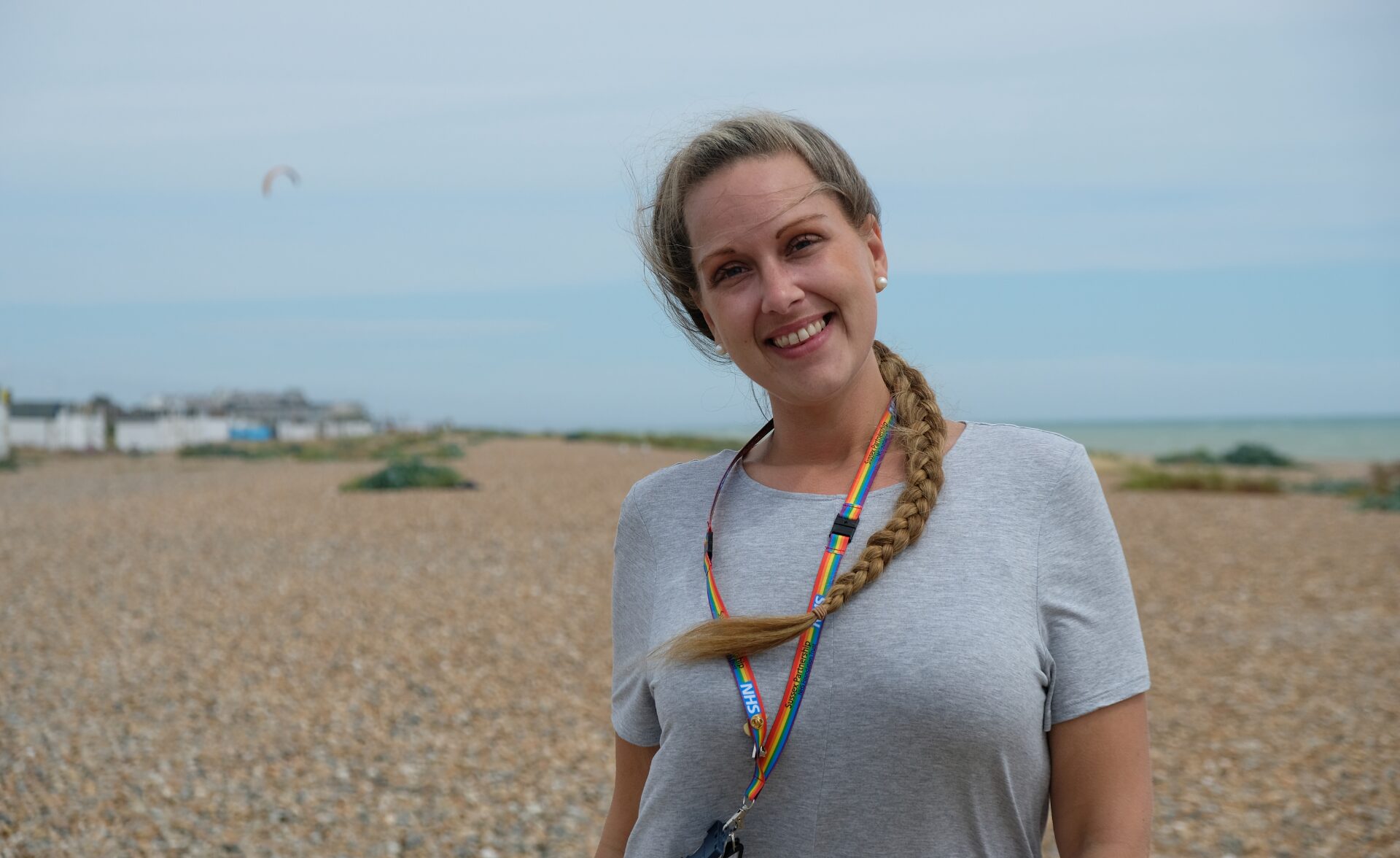 A woman in white tshirt smiles looking at the camera. There is sea in the background