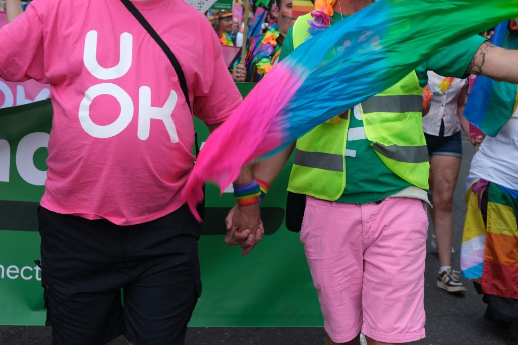 |Photo of UOK Team member stood holding board showing new bright pink UOK logo and web address
