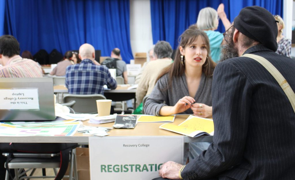 A Recovery College staff member speaks with a visitor at the registration desk during a busy Open Day event