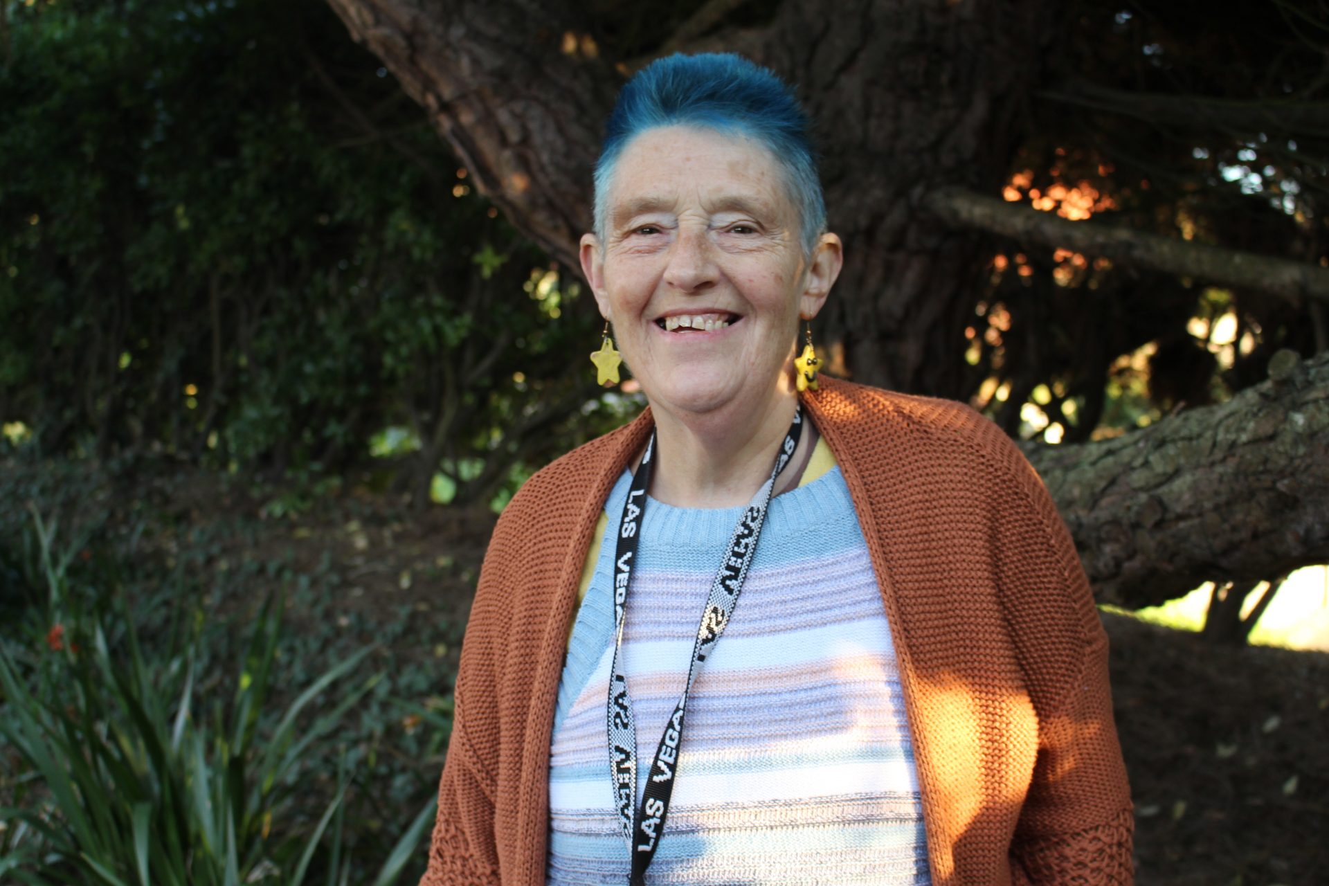 A Support Worker with short blue hair smiles at the camera. She is wearing a dark orange cardigan