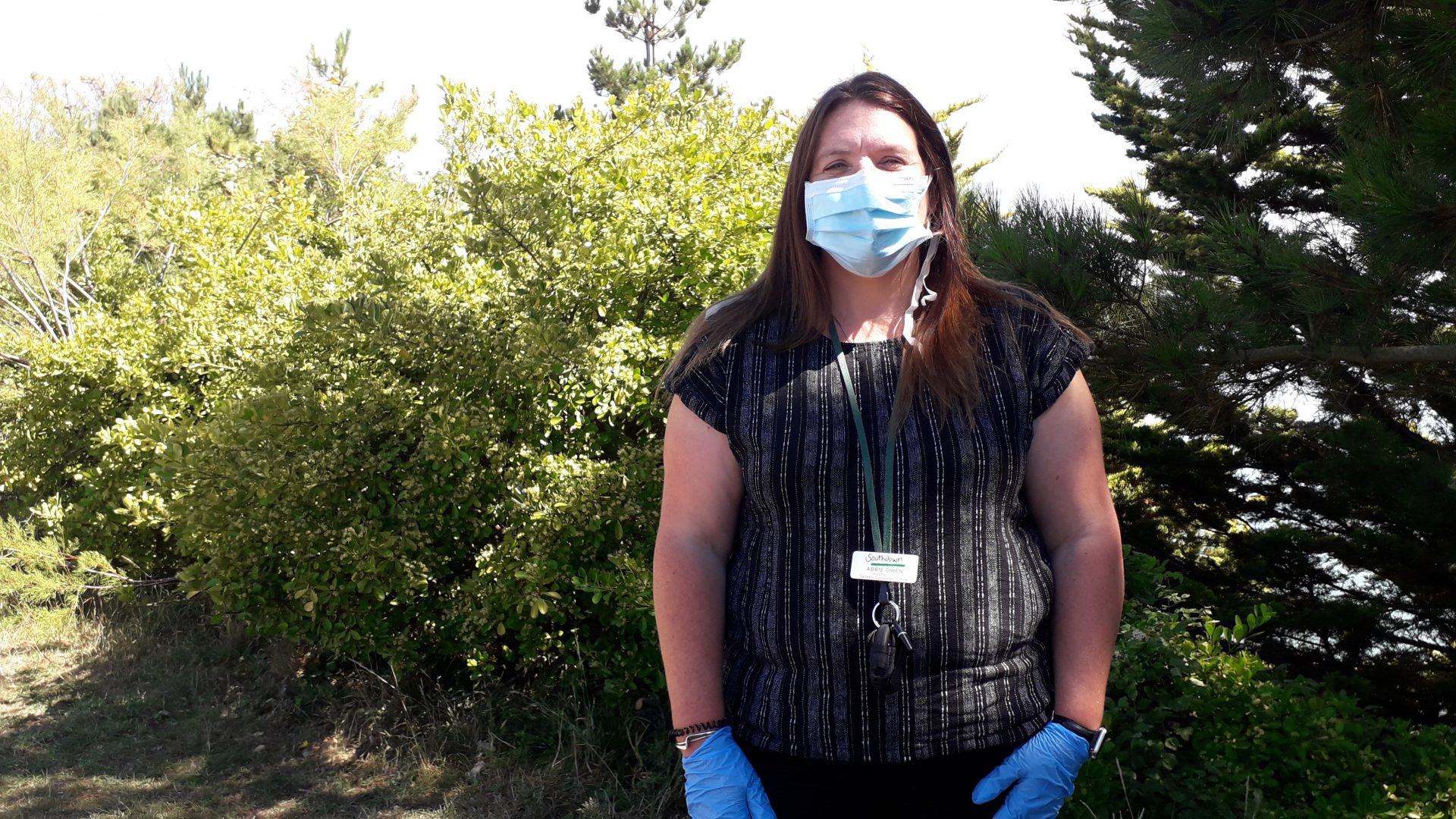 A woman stands outside wearing a mask and gloves