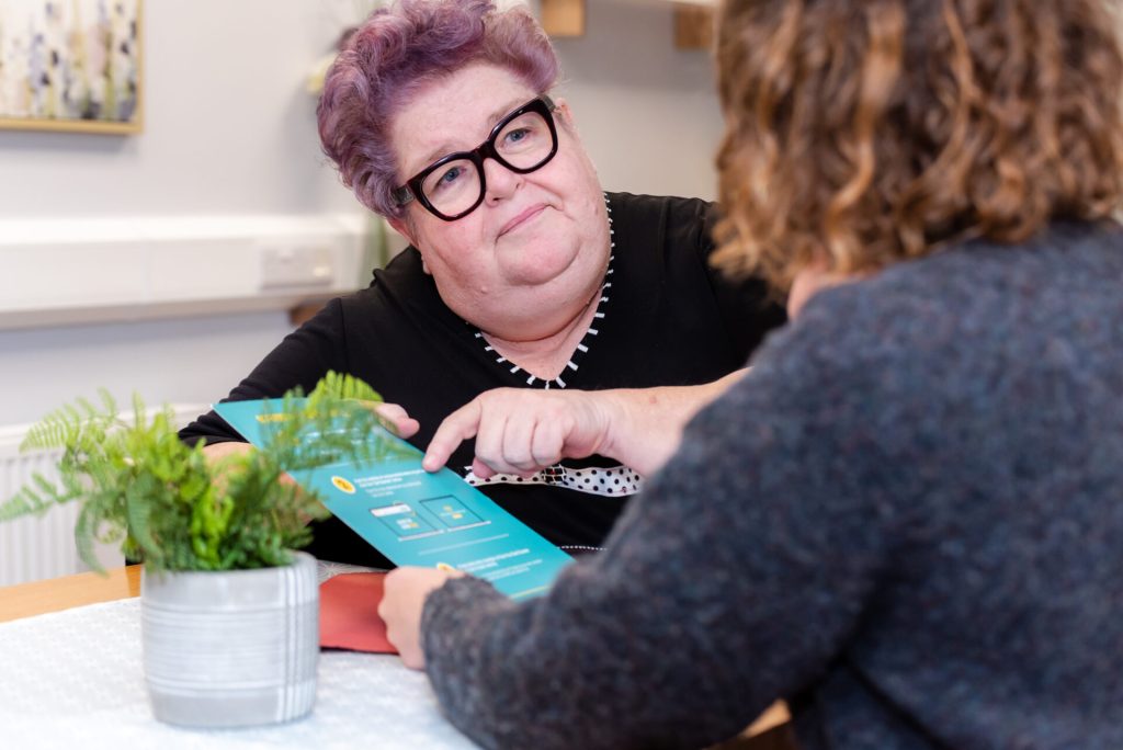 Photo of mental health worker and client sat at table holding a visual document